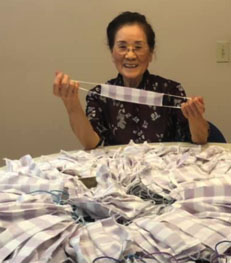 photo of Chin Huang Lan holding up facemask at a table of facemasks